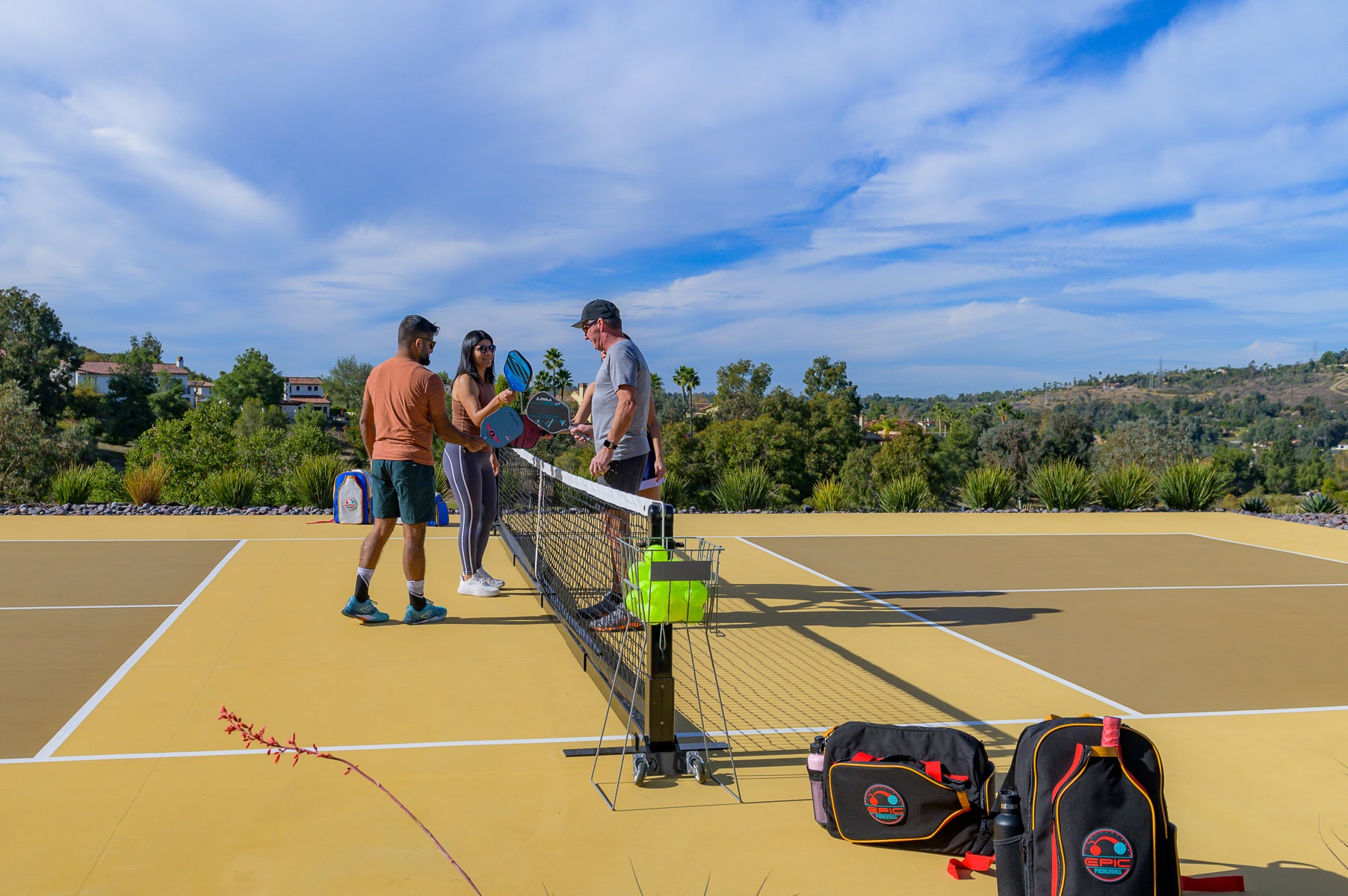 players on an outdoor pickleball court with stylish pickleball bags and premium gear, enjoying a match under a clear sky